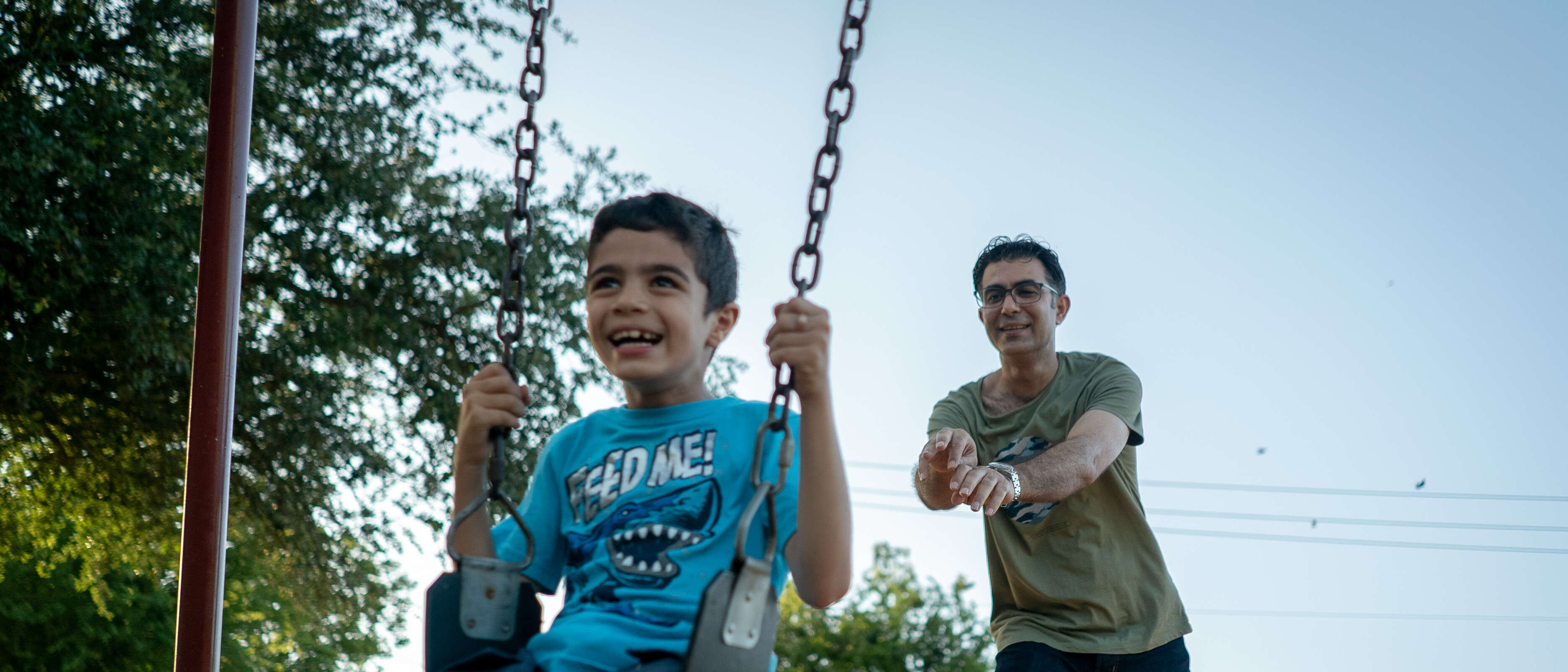 A man pushes a boy in a swing.